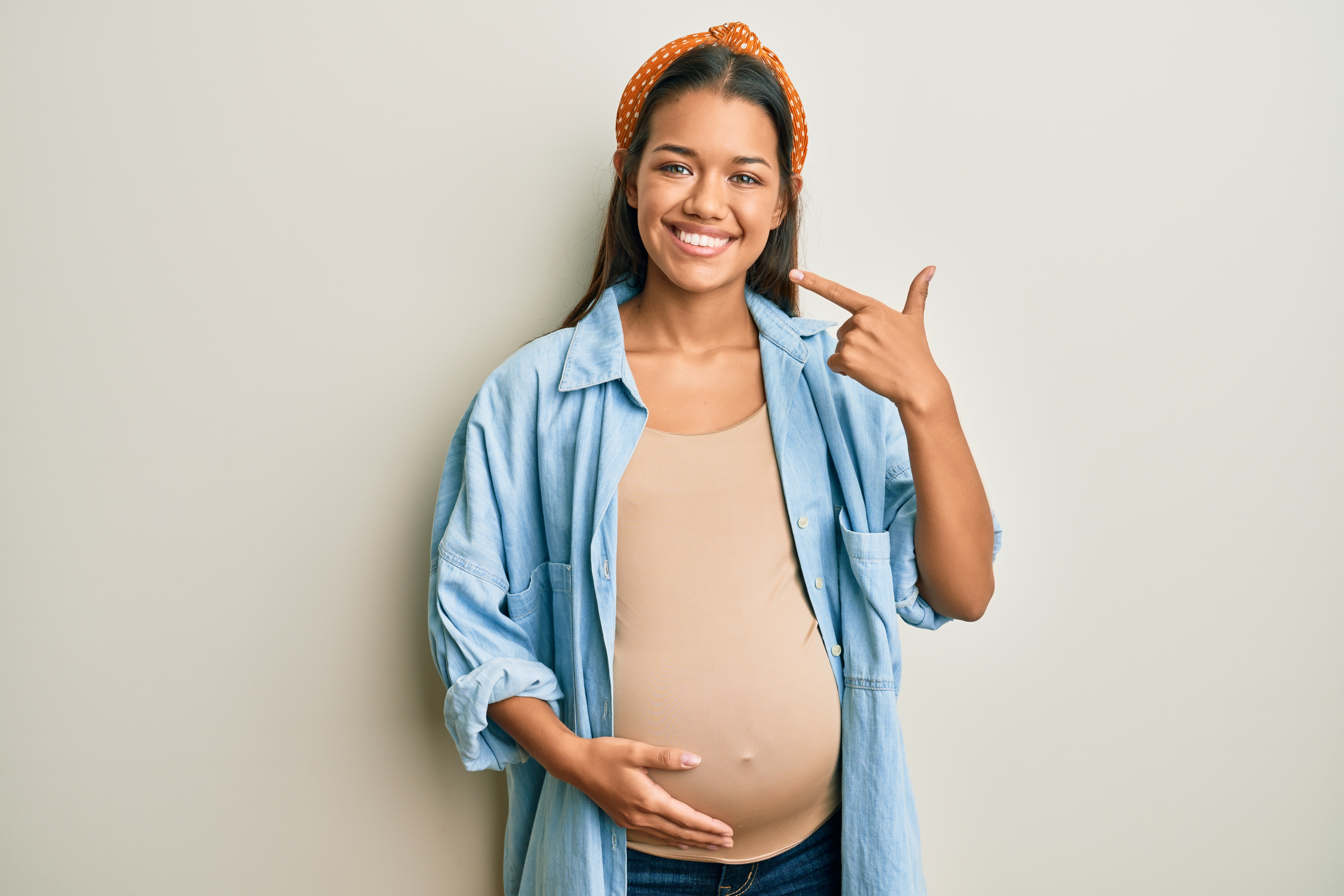 Беременная женщина держится за живот, показывая на свою улыбку.